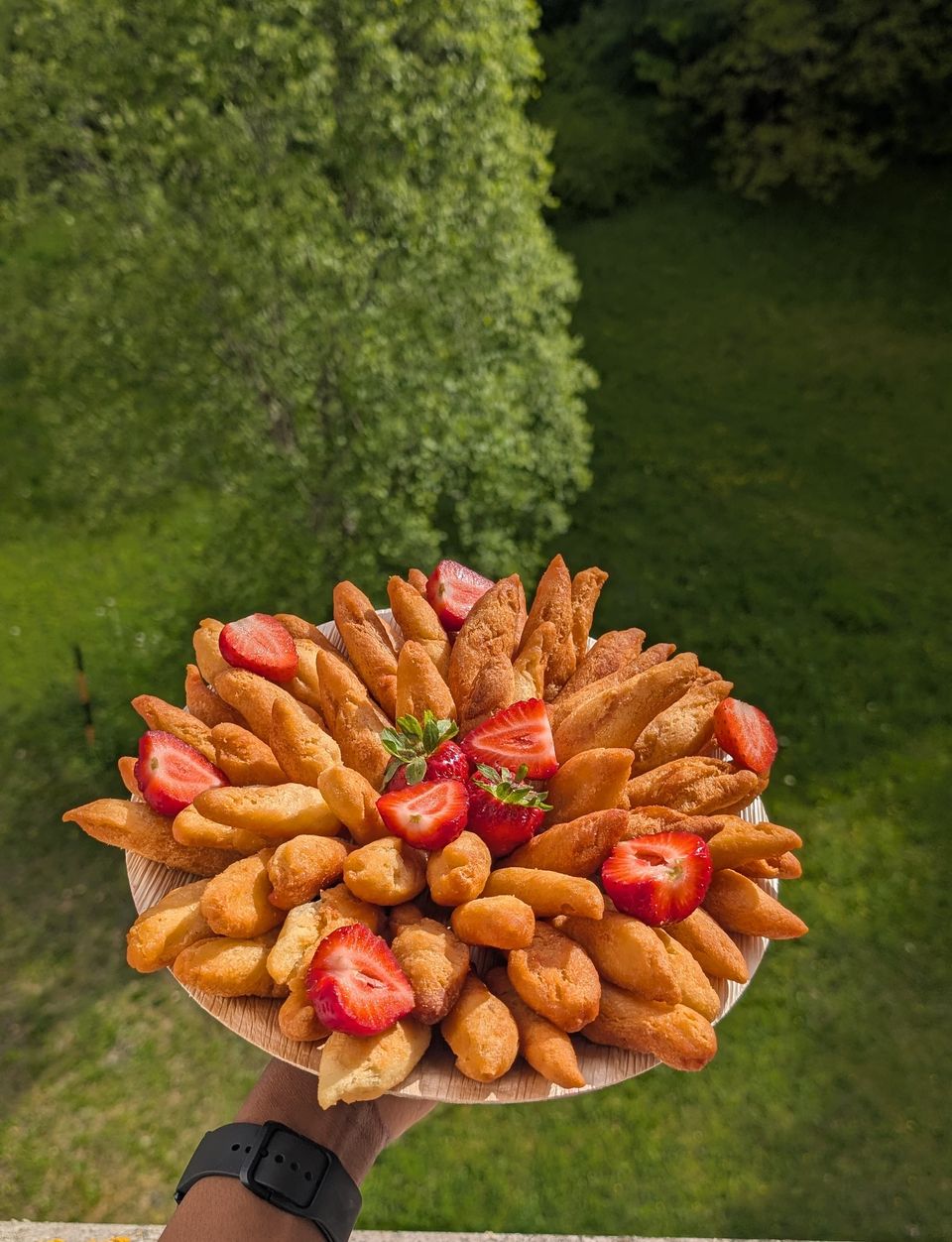 Beignet-Platte mit frischen Erdbeeren, über einem Garten gehalten