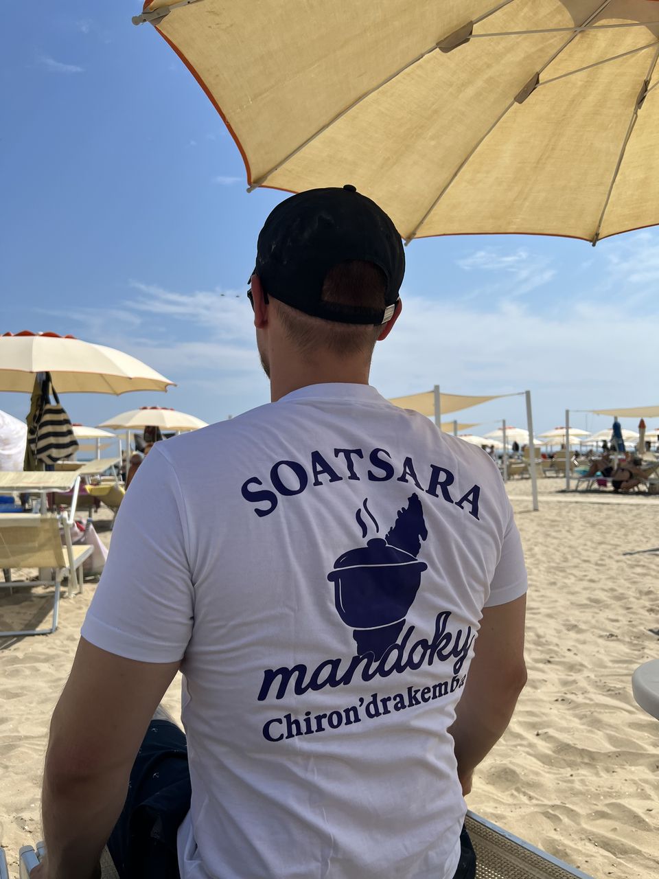 Weißes Soatsara-Mandoky-Shirt mit lila Logo am Strand